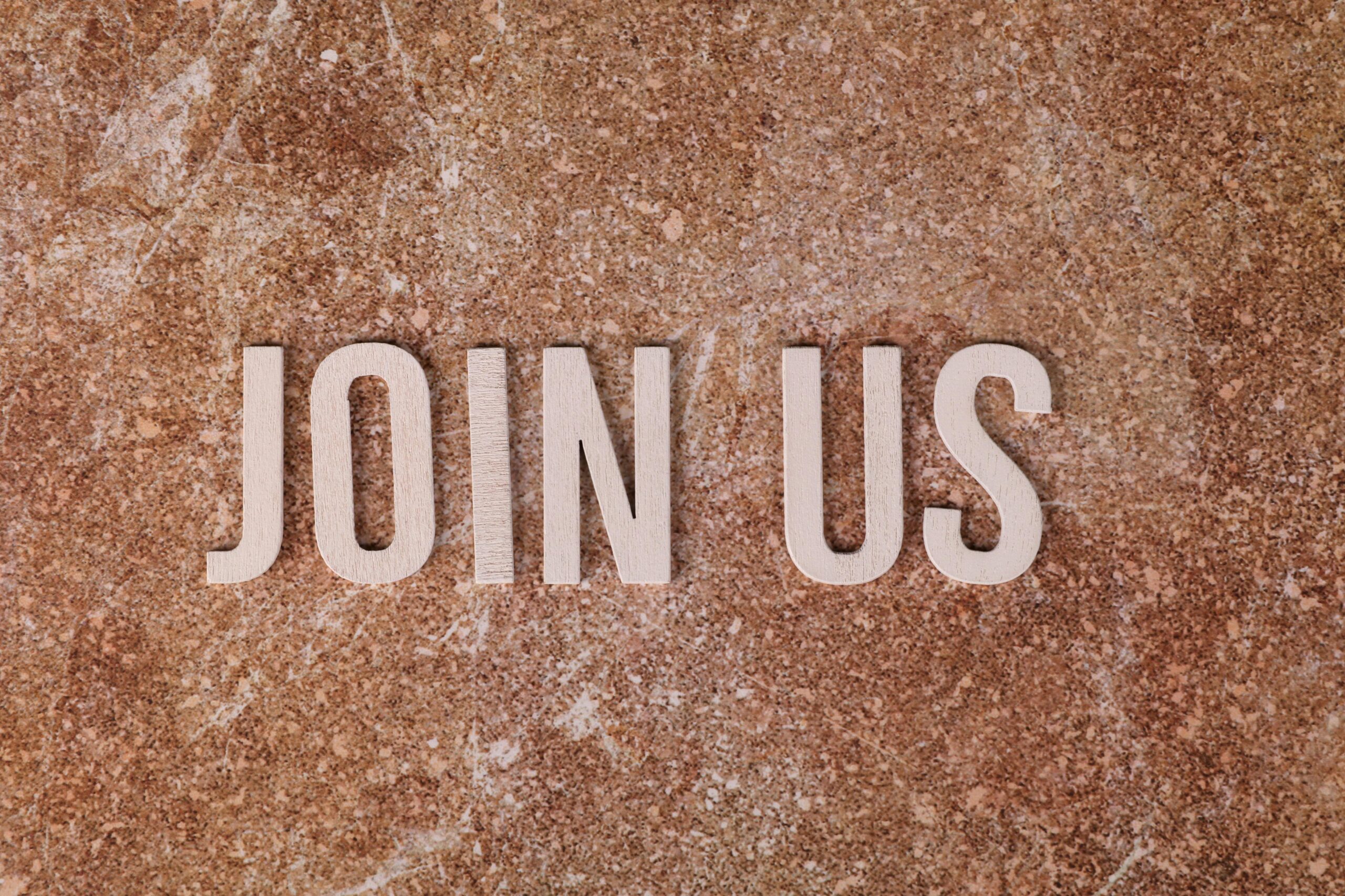 Join Us The words 'Join Us' are spelt out in pink letters on a sandy background