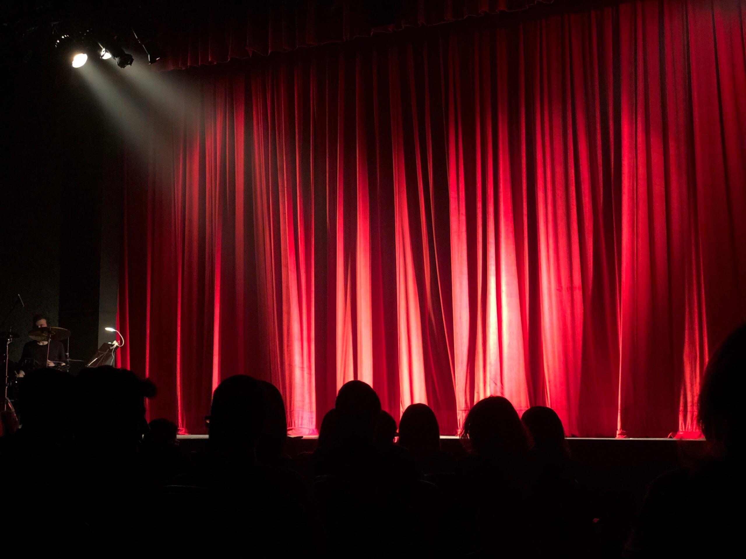 Theatre A spotlight shines on a stage before a performance begins with audience members shown in silhouette