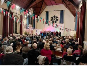 A choir sings in a hall strung with Christmas bunting